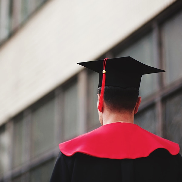 The back view of a male graduate wearing a red stole with his black cap and gown