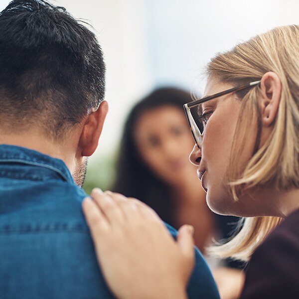 A woman comforting a man with his back to the viewer with a hand on his shoulder