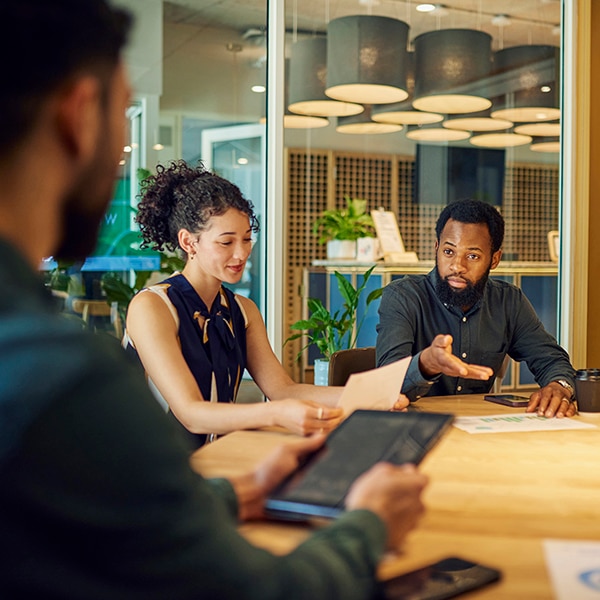 A group of colleagues are sitting around a table in a modern office. They are discussing a business plan and looking at documents.