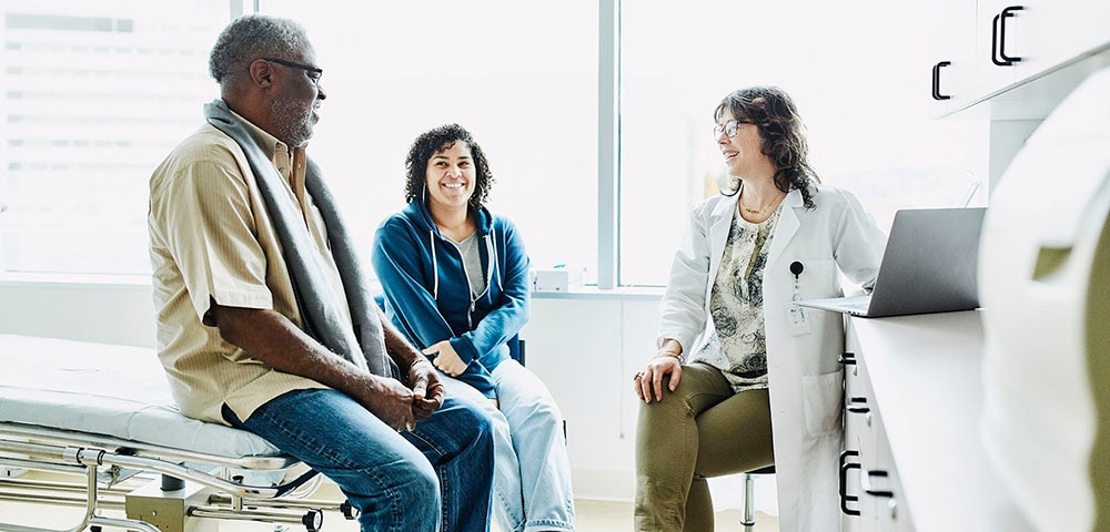 Smiling female doctor consulting with senior male patient and adult daughter in exam room