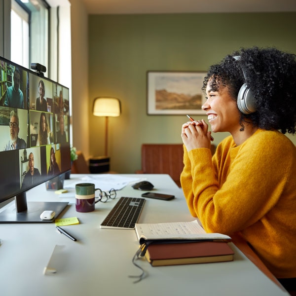 Woman on group video call smiling and holding a pen.