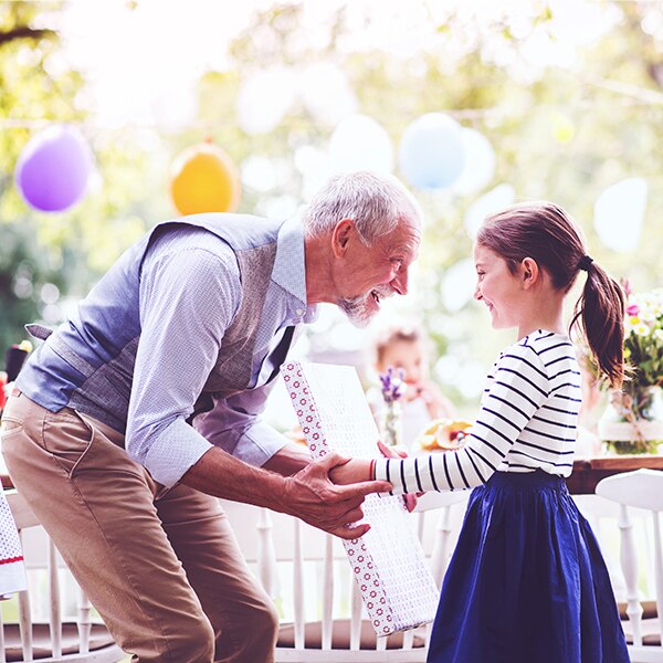 Grandfather talking to granddaughter while handing her gift at party